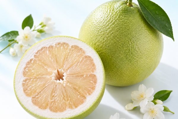 Quả bưởi xanh và nửa quả cắt ngang, bên cạnh có hoa nhài trắng